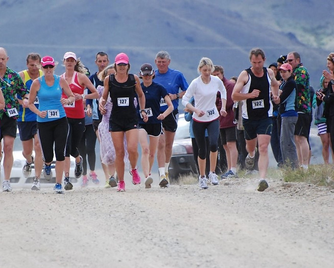 A pack of runners with race bibs start running towards the camera on a gravel road